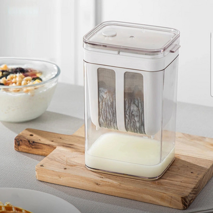 מסננת להכנת גבינות רכות מונחת על קרש עץ, עם נוזל גבינה מסונן שנאסף בחלק התחתון של המיכל השקוף.

